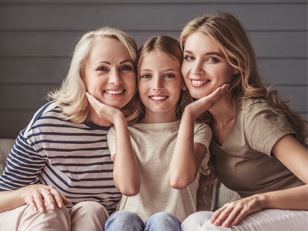 Three women of different generations smiling and leaning together