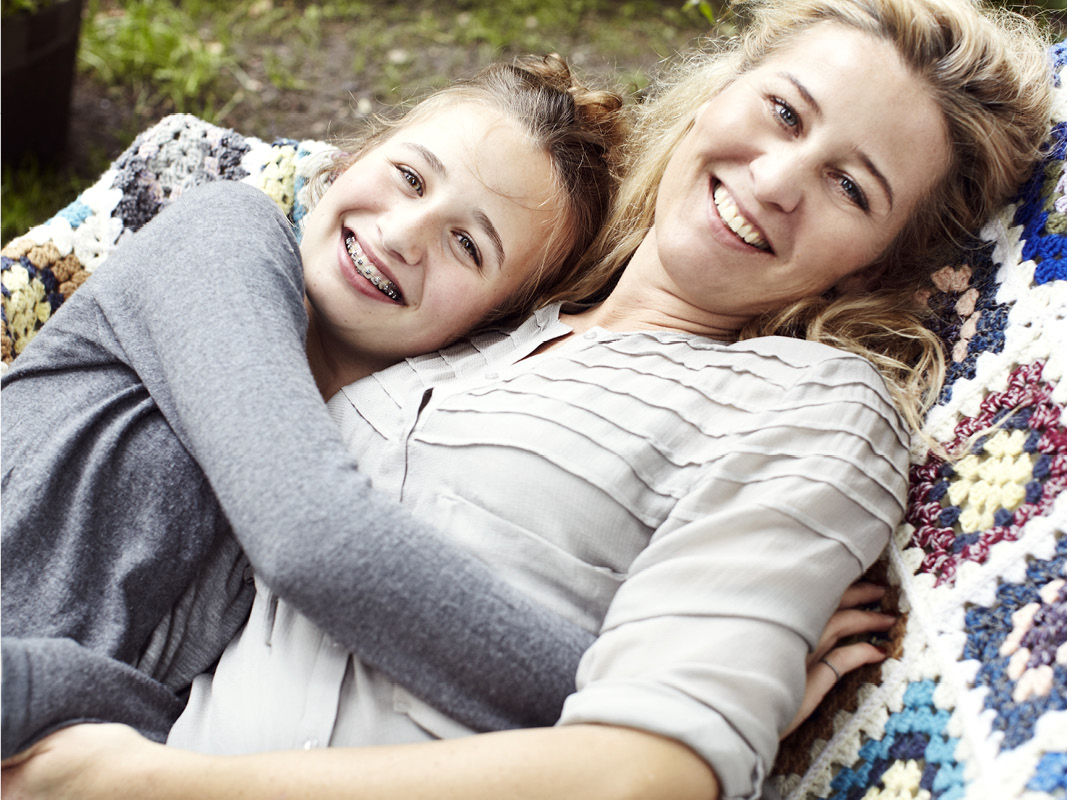 Mother and young girl with braces smiling and snuggling outdoors