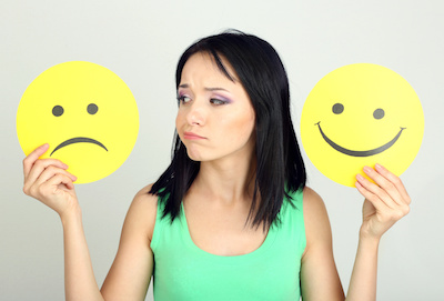 Young woman frowning while holding sad and happy face emojis